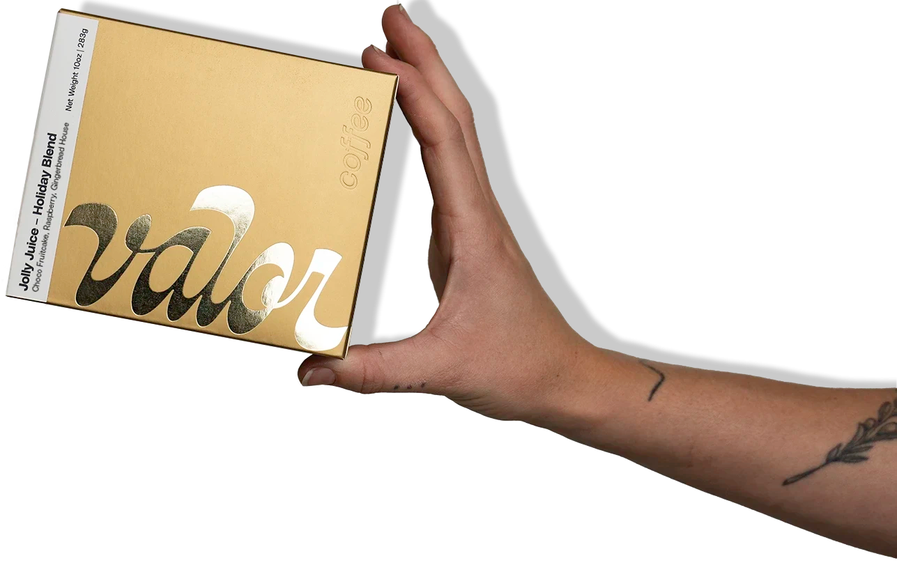 A hand holding a golden box of Valor's holiday blend, Jolly Juice